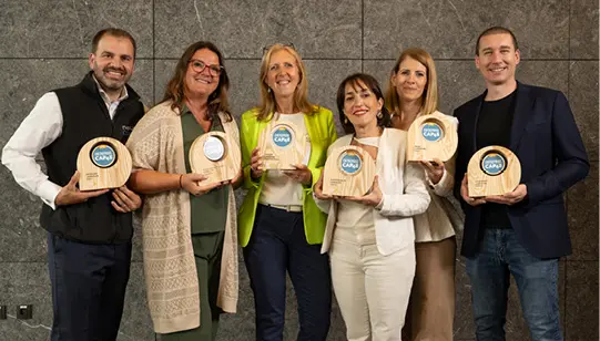 Six personnes debout souriantes tenant des trophées en bois avec un logo bleu dans un cadre intérieur moderne.

Description générée par IA