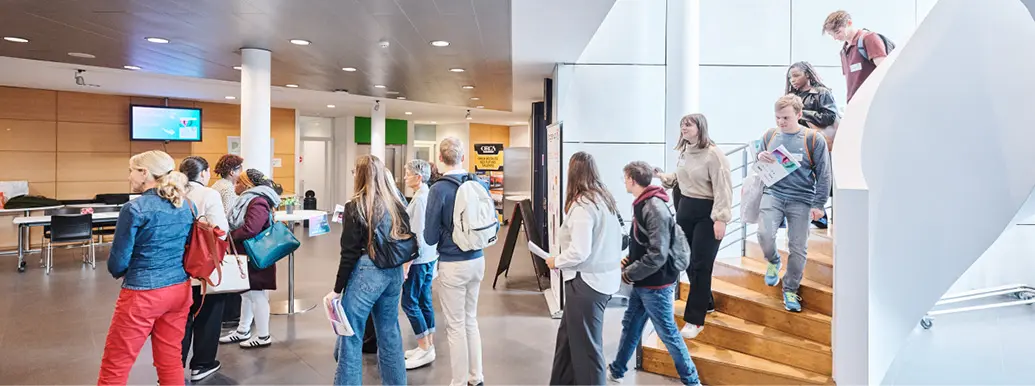Des personnes portant des vêtements décontractés attendent en file dans un espace intérieur moderne avec un escalier et un plafond sombre.

Description générée par IA