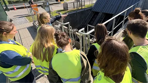 Un groupe de personnes observe attentivement une structure métallique inclinée dans un environnement extérieur ensoleillé.

Description générée par IA