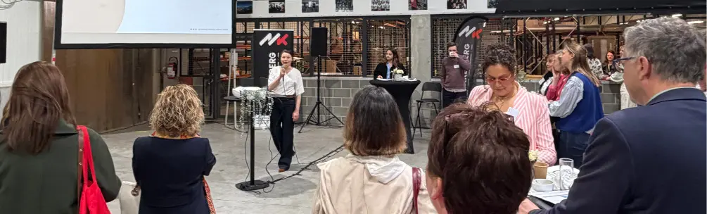 Un groupe de personnes écoute un adulte debout près d'un écran de projection dans un espace industriel avec une bannière affichant le texte « La force de la team ».

Description générée par IA