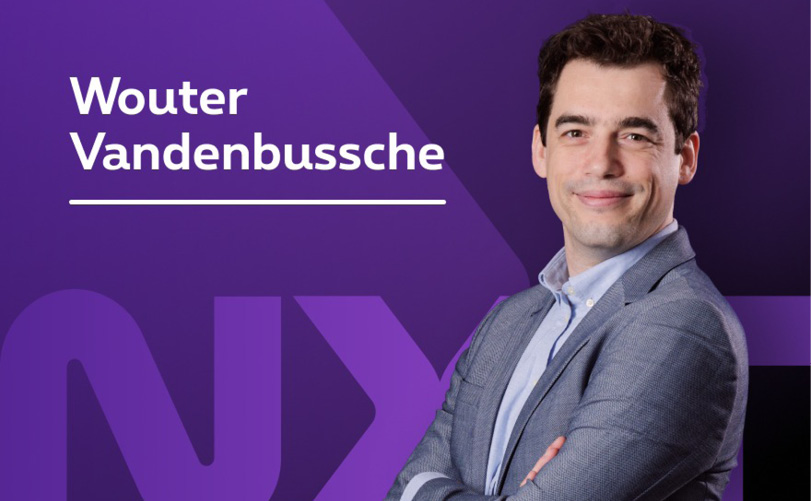 Une personne portant une chemise claire et une veste grise est debout les bras croisés devant un fond violet avec le texte « Wouter Vandenbussche ».

Description générée par IA