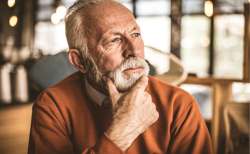 Une personne âgée portant un pull orange est assise dans un intérieur lumineux et semble pensive avec la main posée sur le menton.

Description générée par IA