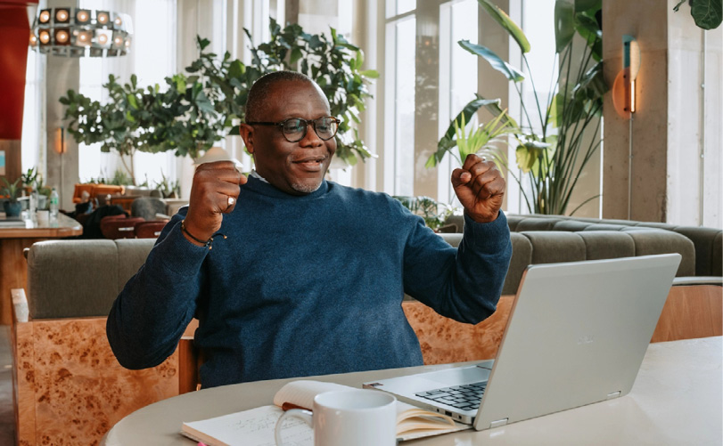 Une personne portant un pull bleu est assise à une table avec un ordinateur portable ouvert, un carnet et une tasse, levant les poings en signe de victoire dans un environnement intérieur lumineux avec des plantes.

Description générée par IA