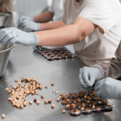 Des personnes portant des gants en latex trient et placent des noisettes dans des moules sur une table métallique dans un environnement de travail.

Description générée par IA