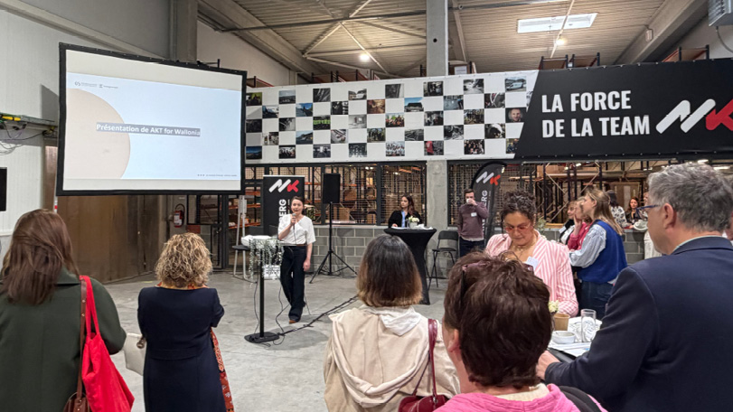 Un groupe de personnes écoute un adulte qui parle au micro devant un écran de projection dans un espace industriel avec une grande bannière affichant « LA FORCE DE LA TEAM ».

Description générée par IA
