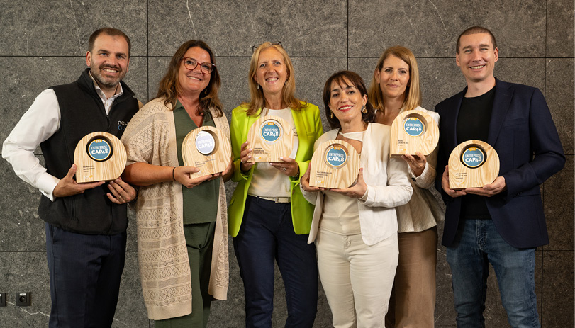 Six personnes debout en tenue décontractée tenant des trophées en bois avec un logo bleu dans un environnement intérieur moderne.

Description générée par IA